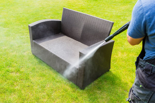 A professional cleaner washing down an outdoor couch.